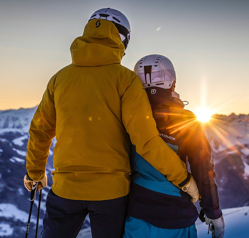 Paar in Skikleidung blickt auf Sonnenuntergang im Skigebiet